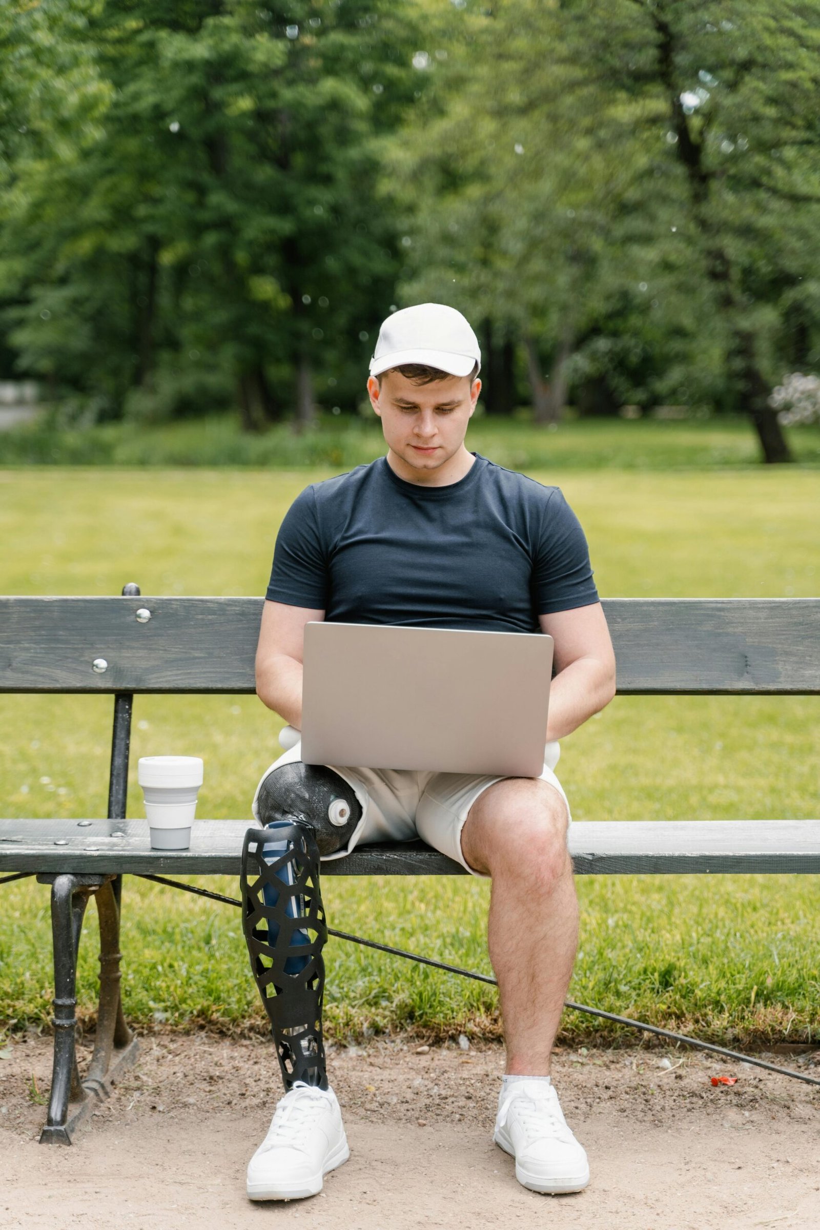 Man Sitting on a Wooden Bench with Prosthetic Leg Using a Computer Laptop